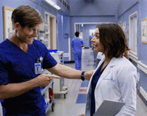 A Man And A Woman Are Standing In A Hospital Hallway GIF