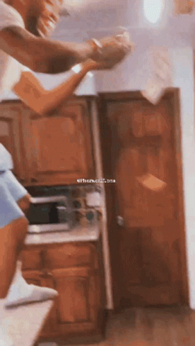 A Man And A Woman Are Standing In A Kitchen Holding Hands While The Woman Throws Papers In The Air . GIF