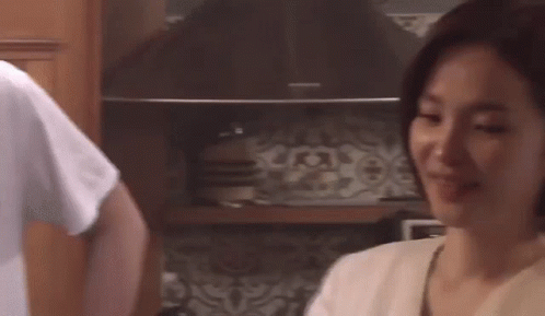 A Man And A Woman Are Standing In A Kitchen . GIF