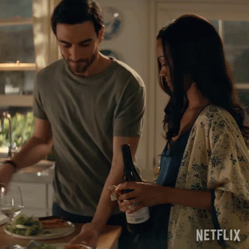 A Man And A Woman Are Standing In A Kitchen With A Bottle Of Wine And A Netflix Logo GIF