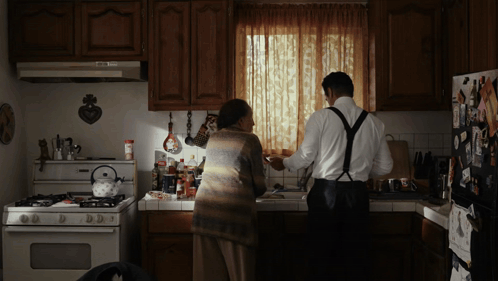 A Man And A Woman Are Standing In A Kitchen GIF