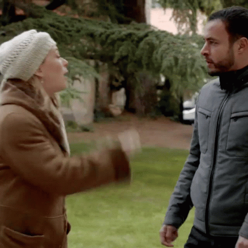 A Man And A Woman Are Standing In A Park GIF