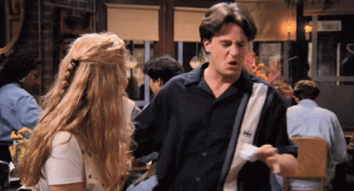A Man And A Woman Are Standing In A Restaurant And The Man Is Wearing A Shirt That Says Hh GIF