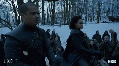 A Man And A Woman Are Standing In A Snowy Forest With The Word Got On The Bottom GIF