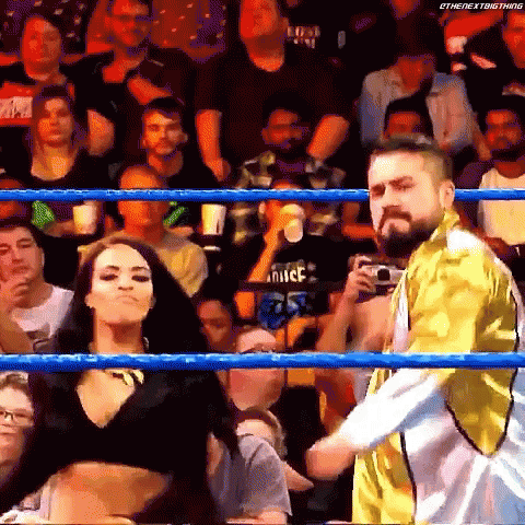 A Man And A Woman Are Standing In A Wrestling Ring With A Crowd Watching . GIF