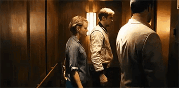 A Man And A Woman Are Standing In An Elevator With A Man Standing Behind Them . GIF