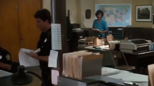 A Man And A Woman Are Standing In An Office With A Map Of The United States In The Background GIF