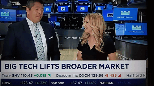 A Man And A Woman Are Standing In Front Of A Big Tech Lifts Broader Market Banner GIF