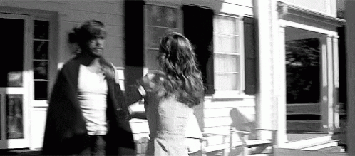 A Man And A Woman Are Standing In Front Of A House . GIF