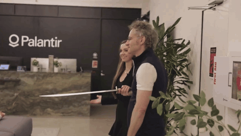 A Man And A Woman Are Standing In Front Of A Palantir Sign GIF