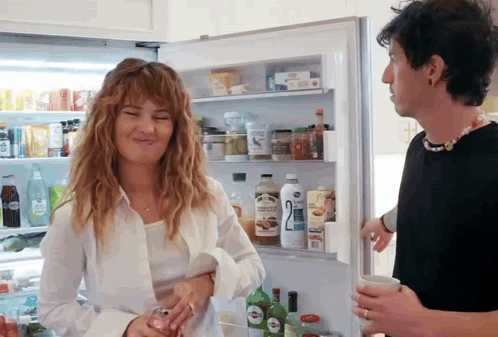 A Man And A Woman Are Standing In Front Of A Refrigerator With The Number 2 On The Bottle GIF