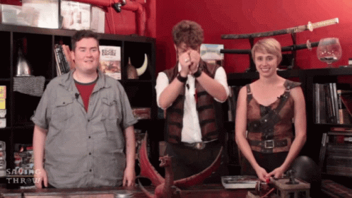 A Man And A Woman Are Standing In Front Of A Shelf With A Book Titled Saving Throw GIF