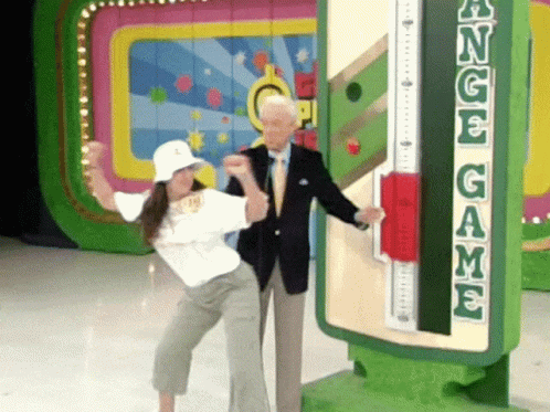 A Man And A Woman Are Standing In Front Of A Sign That Says Angel Game GIF