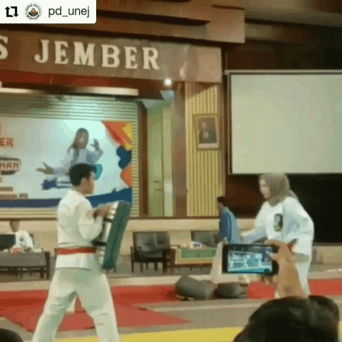 A Man And A Woman Are Standing In Front Of A Sign That Says ' S Jember ' On It GIF