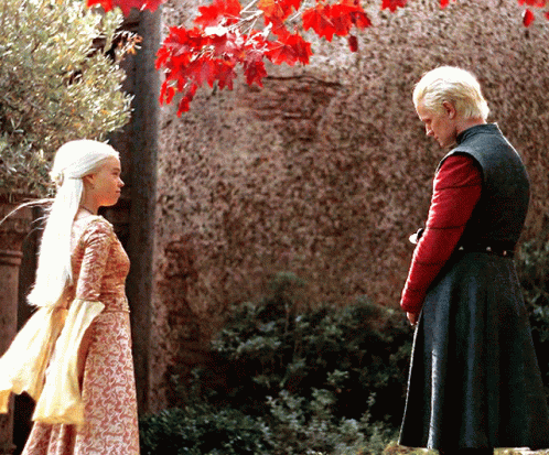 A Man And A Woman Are Standing In Front Of A Stone Wall GIF