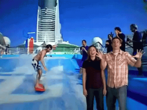 A Man And A Woman Are Standing In Front Of A Wave Pool While A Man Rides A Surfboard GIF