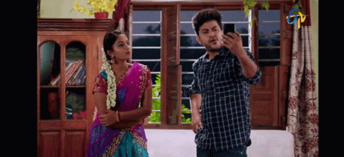 A Man And A Woman Are Standing In Front Of A Window . GIF