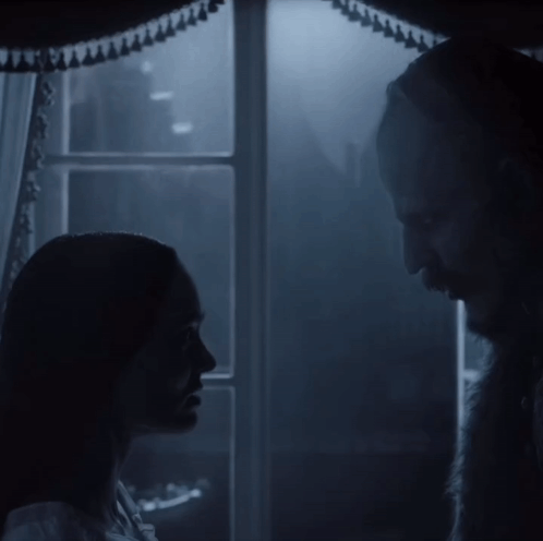 A Man And A Woman Are Standing In Front Of A Window GIF