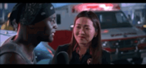 A Man And A Woman Are Standing In Front Of An Ambulance . GIF