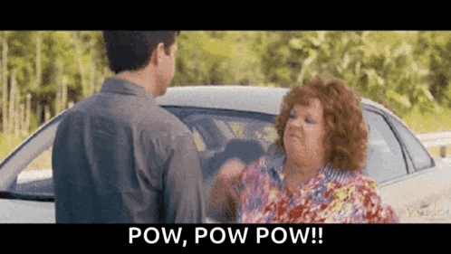 A Man And A Woman Are Standing Next To A Car And The Woman Is Saying Pow , Pow Pow ! GIF