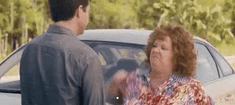 A Man And A Woman Are Standing Next To A Car . GIF