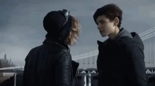 A Man And A Woman Are Standing Next To Each Other And Looking At Each Other In Front Of A Bridge . GIF