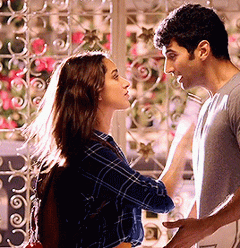 A Man And A Woman Are Standing Next To Each Other And Looking At Each Other In Front Of A Window . GIF