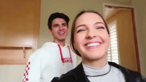 A Man And A Woman Are Standing Next To Each Other And Smiling . The Woman Is Wearing A Vans Sweatshirt . GIF