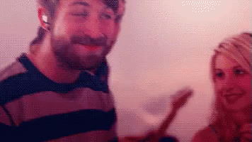 A Man And A Woman Are Standing Next To Each Other And The Man Is Wearing Headphones GIF