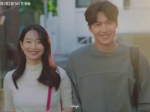 A Man And A Woman Are Standing Next To Each Other And The Woman Has A Pink Purse On Her Shoulder And The Man Is Smiling GIF