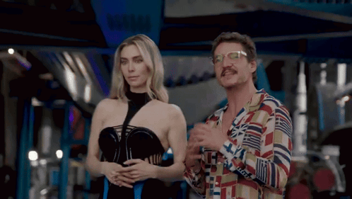 A Man And A Woman Are Standing Next To Each Other And The Woman Is Wearing A Black Dress GIF