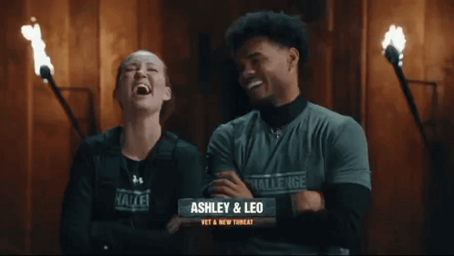 A Man And A Woman Are Standing Next To Each Other And The Woman Is Wearing A Challenge Shirt GIF
