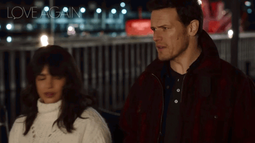 A Man And A Woman Are Standing Next To Each Other And The Words Love Again Are Visible In The Background GIF