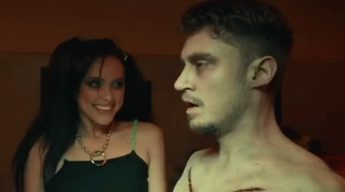 A Man And A Woman Are Standing Next To Each Other In A Dark Room And Smiling . GIF