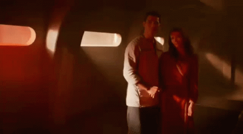 A Man And A Woman Are Standing Next To Each Other In A Dark Room Holding Hands . GIF
