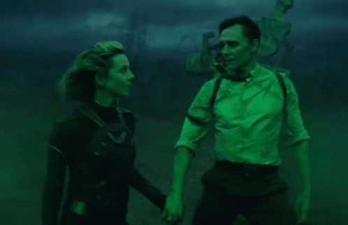 A Man And A Woman Are Standing Next To Each Other In A Dark Room Holding Hands . GIF