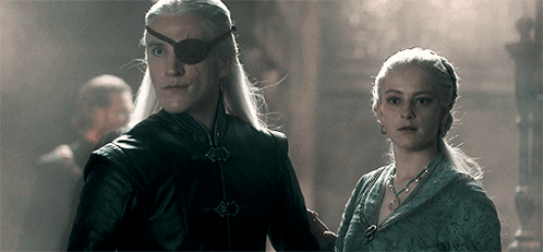 A Man And A Woman Are Standing Next To Each Other In A Dark Room . The Man Is Wearing An Eye Patch . GIF