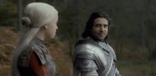A Man And A Woman Are Standing Next To Each Other In A Forest . GIF