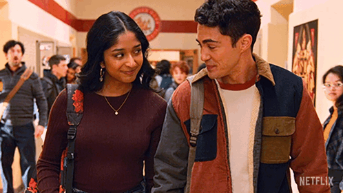 A Man And A Woman Are Standing Next To Each Other In A Hallway And Looking At Each Other . GIF