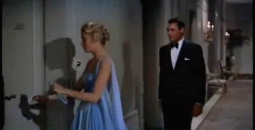 A Man And A Woman Are Standing Next To Each Other In A Hallway . The Woman Is Wearing A Blue Dress . GIF