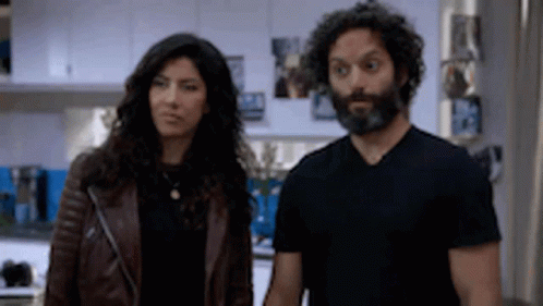 A Man And A Woman Are Standing Next To Each Other In A Kitchen . The Woman Is Wearing A Leather Jacket . GIF