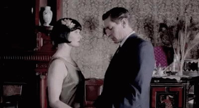 A Man And A Woman Are Standing Next To Each Other In A Living Room And Holding Hands . GIF
