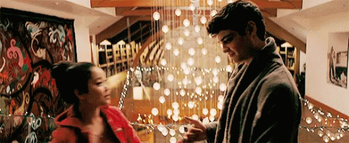 A Man And A Woman Are Standing Next To Each Other In A Living Room In Front Of A Christmas Tree . GIF