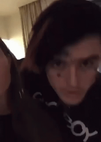A Man And A Woman Are Standing Next To Each Other In A Room And Looking At The Camera . GIF