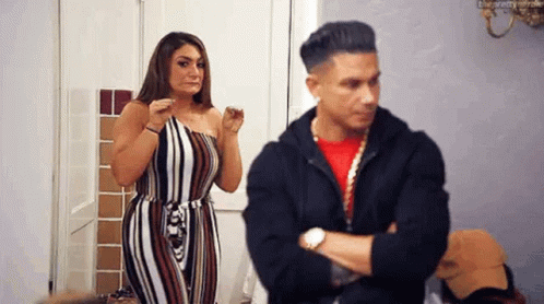 A Man And A Woman Are Standing Next To Each Other In A Room . The Man Is Looking At The Woman . GIF