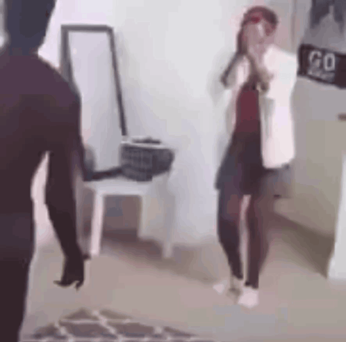 A Man And A Woman Are Standing Next To Each Other In A Room . The Woman Is Covering Her Face With Her Hands . GIF