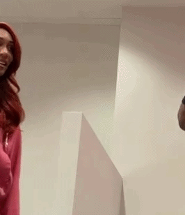 A Man And A Woman Are Standing Next To Each Other In A Room . The Woman Is Wearing A Pink Sweater . GIF