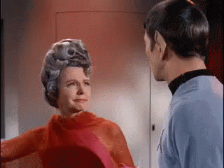 A Man And A Woman Are Standing Next To Each Other In A Room . The Woman Is Wearing A Red Dress . GIF