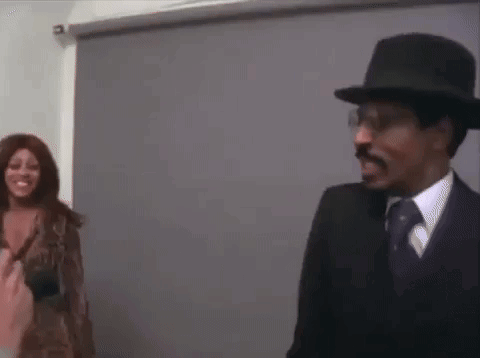 A Man And A Woman Are Standing Next To Each Other In A Room . The Woman Is Wearing A Wig . GIF