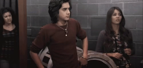 A Man And A Woman Are Standing Next To Each Other In A Room With A Brick Wall . GIF
